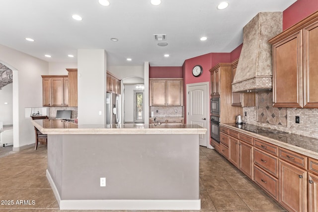 kitchen featuring black appliances, custom exhaust hood, tasteful backsplash, a kitchen island with sink, and tile patterned flooring