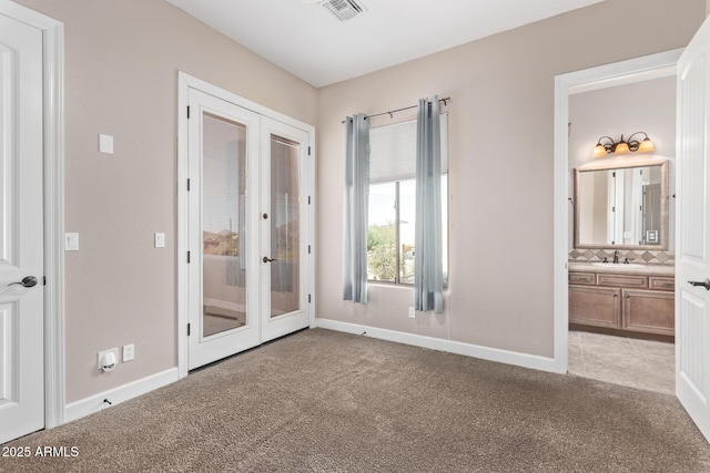 unfurnished bedroom featuring sink, ensuite bathroom, light carpet, and french doors