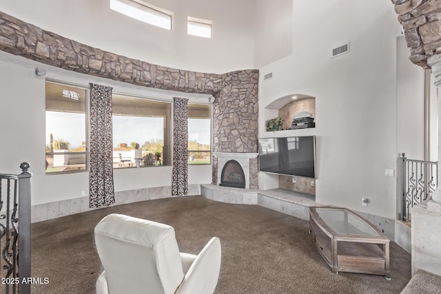 living room featuring a towering ceiling, carpet floors, built in shelves, ornate columns, and a stone fireplace