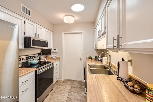 kitchen with a sink, stainless steel appliances, visible vents, white cabinetry, and light countertops