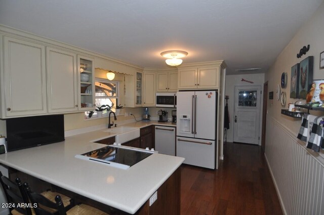 kitchen featuring white appliances, a peninsula, light countertops, glass insert cabinets, and dark wood-style flooring