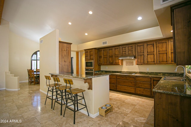 kitchen with sink, a kitchen bar, stainless steel appliances, and dark stone countertops