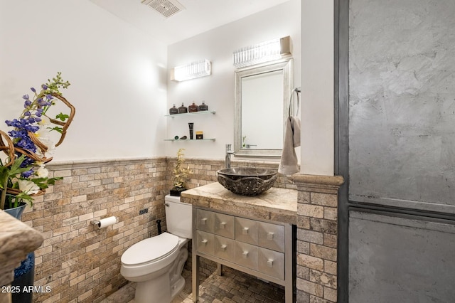 bathroom with toilet, vanity, visible vents, tile walls, and wainscoting