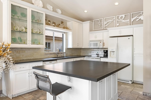 kitchen featuring white appliances, dark countertops, a sink, and stone tile flooring