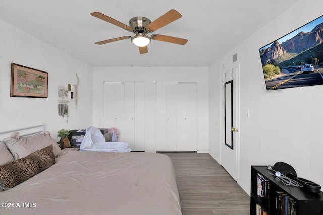 bedroom featuring wood finished floors, two closets, visible vents, and a ceiling fan