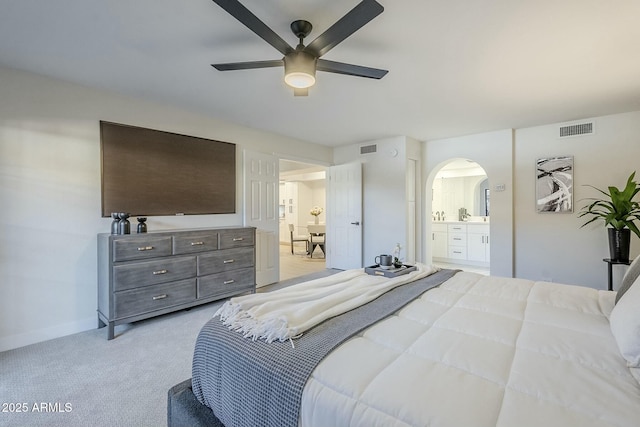 bedroom featuring light colored carpet, ensuite bath, and ceiling fan