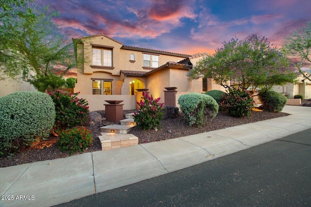 mediterranean / spanish-style home with concrete driveway, a tile roof, and stucco siding