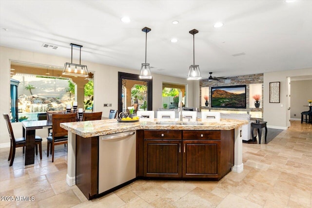 kitchen with sink, light stone counters, hanging light fixtures, a center island with sink, and stainless steel dishwasher