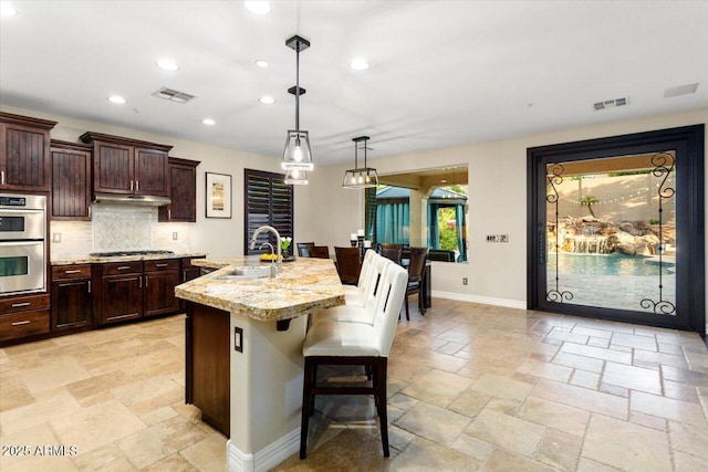 kitchen featuring a breakfast bar, sink, decorative light fixtures, appliances with stainless steel finishes, and an island with sink