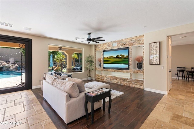 living area featuring stone tile floors, baseboards, visible vents, a ceiling fan, and a textured ceiling