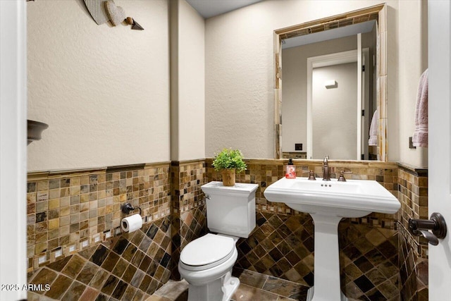 half bathroom featuring toilet, a wainscoted wall, and tile walls