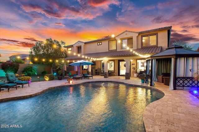 back of house featuring a fenced in pool, a tile roof, stucco siding, a gazebo, and a patio area