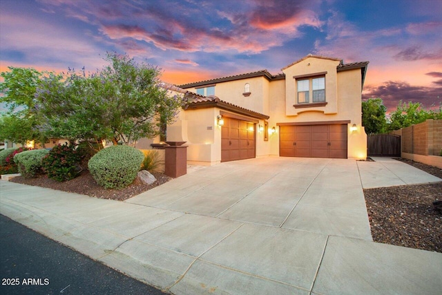 mediterranean / spanish-style home featuring a garage, concrete driveway, a tiled roof, fence, and stucco siding