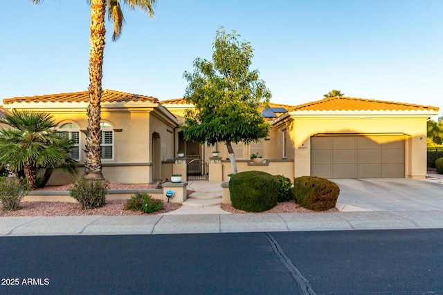 mediterranean / spanish-style home featuring a garage, stucco siding, roof mounted solar panels, concrete driveway, and a tiled roof