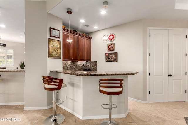 kitchen with a kitchen breakfast bar, decorative backsplash, light tile patterned flooring, and dark stone countertops