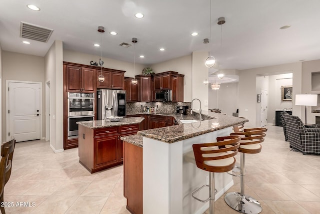 kitchen featuring visible vents, a peninsula, stone countertops, a sink, and stainless steel appliances
