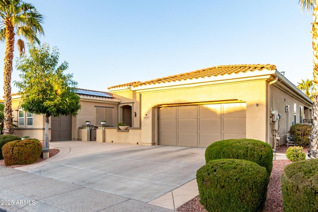 mediterranean / spanish-style home with a tiled roof, driveway, a garage, roof mounted solar panels, and stucco siding