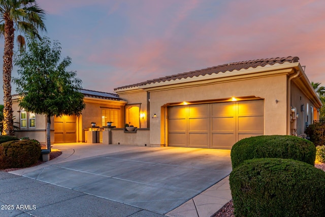 mediterranean / spanish home featuring a tiled roof, driveway, solar panels, a garage, and stucco siding