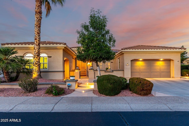 mediterranean / spanish home featuring a garage, driveway, a gate, and stucco siding