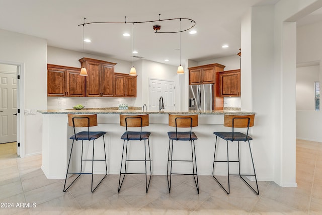 kitchen featuring a breakfast bar area, stainless steel fridge, light stone counters, and light tile patterned floors