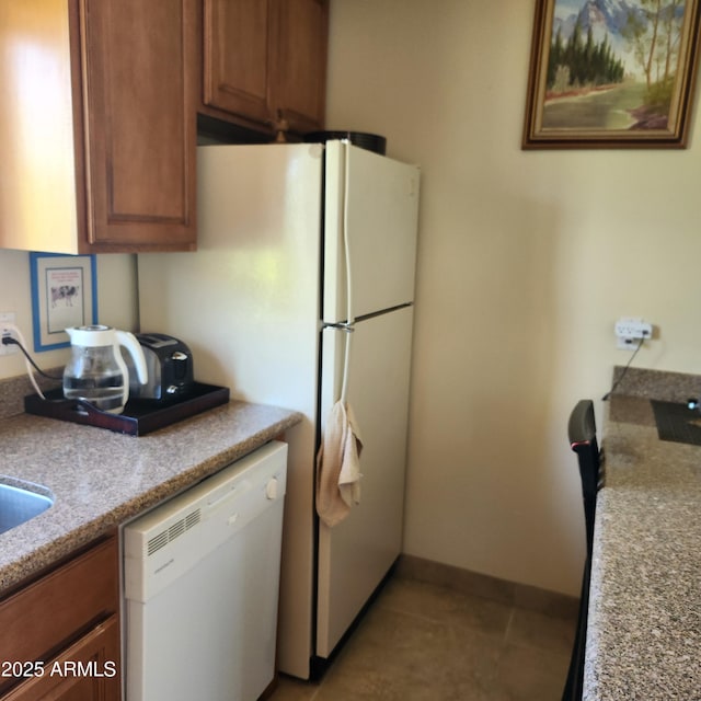 kitchen featuring dishwasher, brown cabinetry, light tile patterned floors, and baseboards