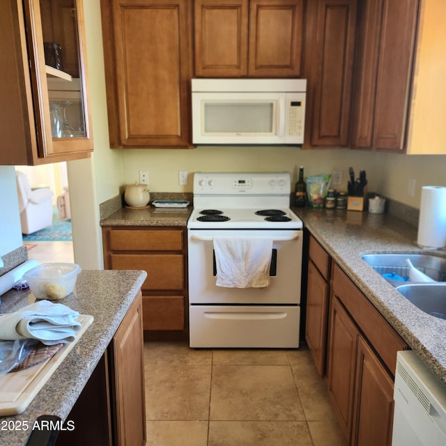kitchen featuring white appliances, brown cabinetry, glass insert cabinets, and a sink