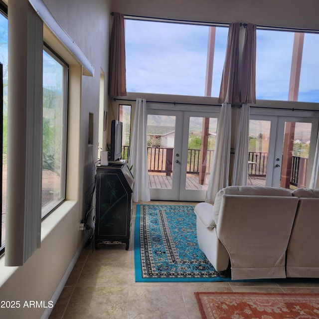 living area with french doors, baseboards, plenty of natural light, and a high ceiling