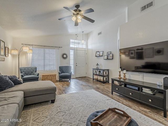 living area with a ceiling fan, wood finished floors, visible vents, and vaulted ceiling