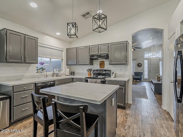 kitchen with a ceiling fan, under cabinet range hood, vaulted ceiling, light countertops, and electric range