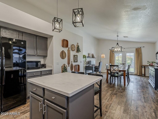 kitchen featuring vaulted ceiling, a breakfast bar, dark wood-type flooring, black appliances, and light countertops