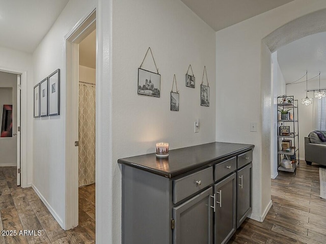hallway with arched walkways, baseboards, and dark wood-type flooring