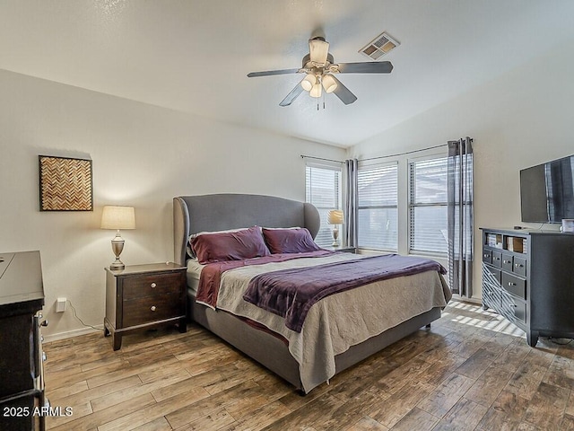 bedroom with a ceiling fan, vaulted ceiling, visible vents, and wood finished floors
