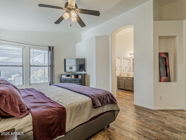 bedroom with a ceiling fan, wood-type flooring, ensuite bathroom, baseboards, and arched walkways