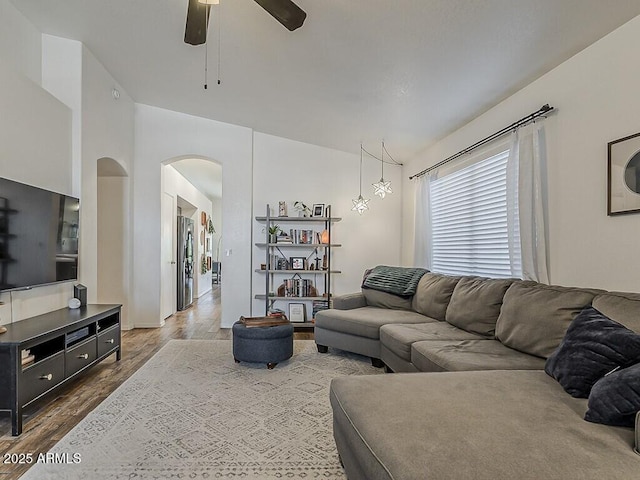 living room with dark wood-type flooring, a ceiling fan, and arched walkways