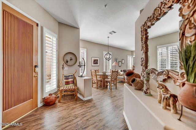 foyer featuring wood finished floors, baseboards, visible vents, an inviting chandelier, and a textured ceiling