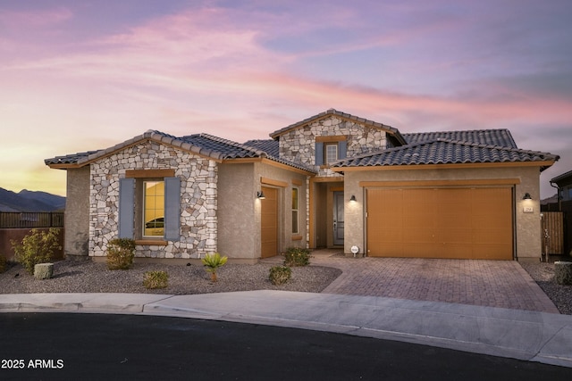 view of front of home with a garage, stone siding, a tiled roof, decorative driveway, and stucco siding