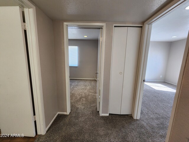 hallway featuring a textured ceiling and dark colored carpet