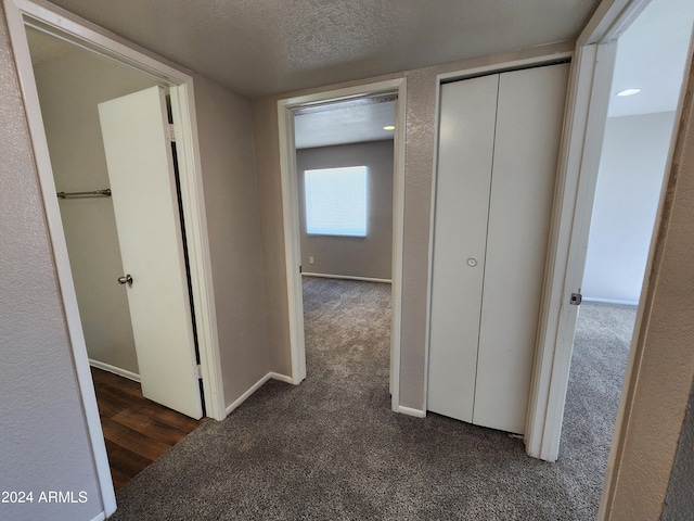 hallway featuring a textured ceiling and dark colored carpet