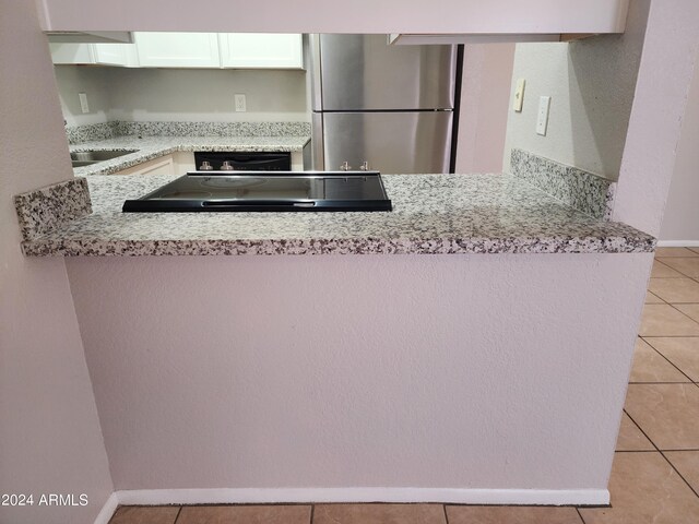 kitchen featuring light stone countertops, white cabinets, light tile patterned floors, and stainless steel fridge