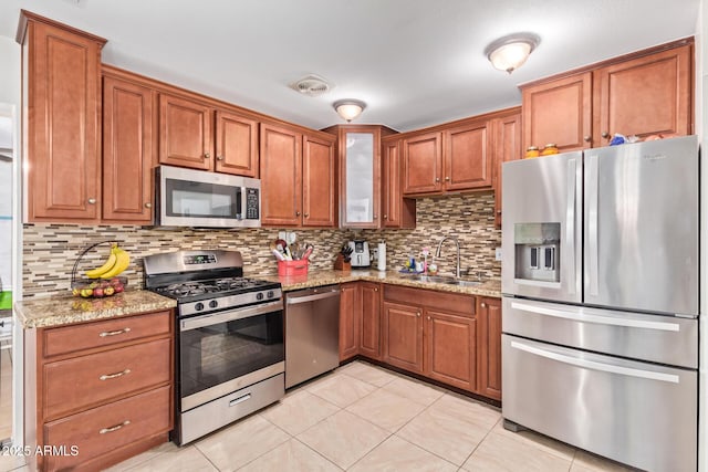 kitchen featuring tasteful backsplash, light stone countertops, appliances with stainless steel finishes, and sink