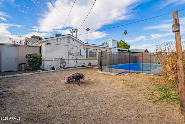 rear view of property featuring a fenced in pool, a fire pit, a yard, and a storage unit