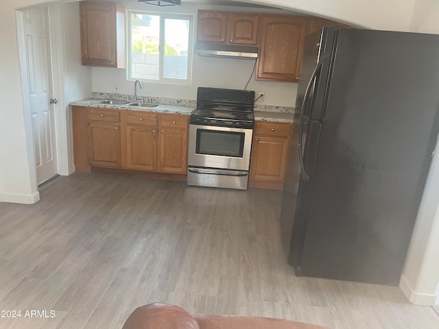 kitchen featuring light stone counters, light hardwood / wood-style floors, sink, black refrigerator, and stainless steel range