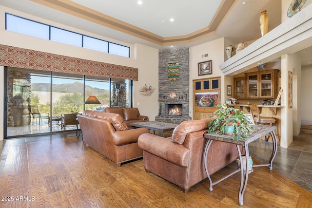 living room featuring hardwood / wood-style flooring, a high ceiling, a mountain view, a tray ceiling, and a stone fireplace