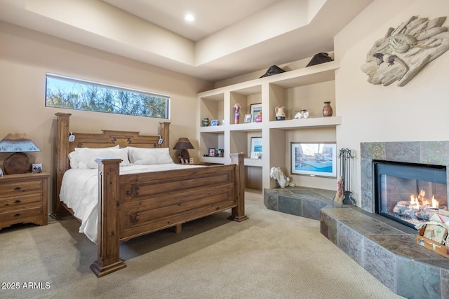 bedroom featuring a fireplace, a tray ceiling, and light colored carpet