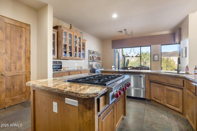 kitchen featuring stainless steel gas cooktop, light stone countertops, dishwashing machine, a kitchen island, and sink