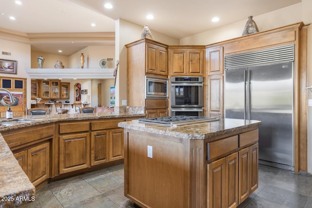 kitchen with built in appliances, light stone countertops, kitchen peninsula, a kitchen island, and sink