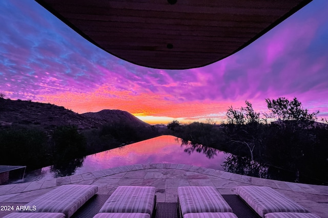 pool at dusk with a patio area and a water view