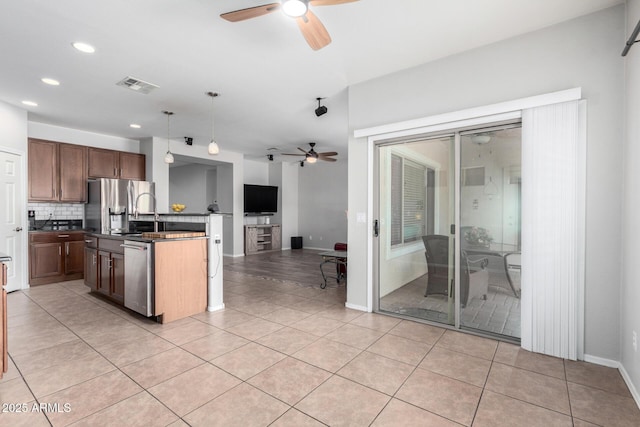 kitchen featuring pendant lighting, stainless steel appliances, tasteful backsplash, light tile patterned floors, and a center island with sink