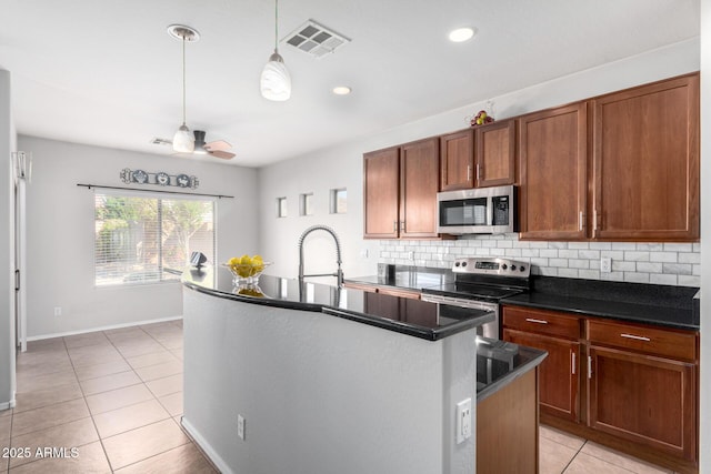 kitchen with stainless steel appliances, decorative backsplash, sink, ceiling fan, and a center island with sink