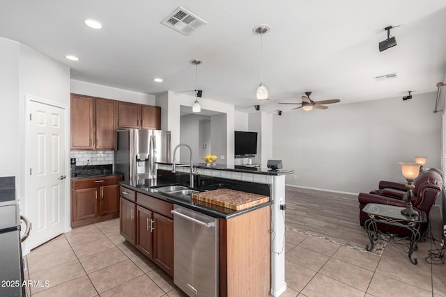 kitchen with ceiling fan, decorative light fixtures, a center island with sink, sink, and stainless steel appliances